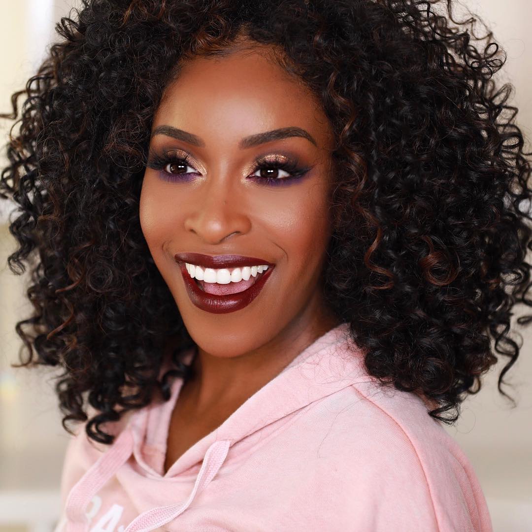 Jackie Aina smiling with curly hair.